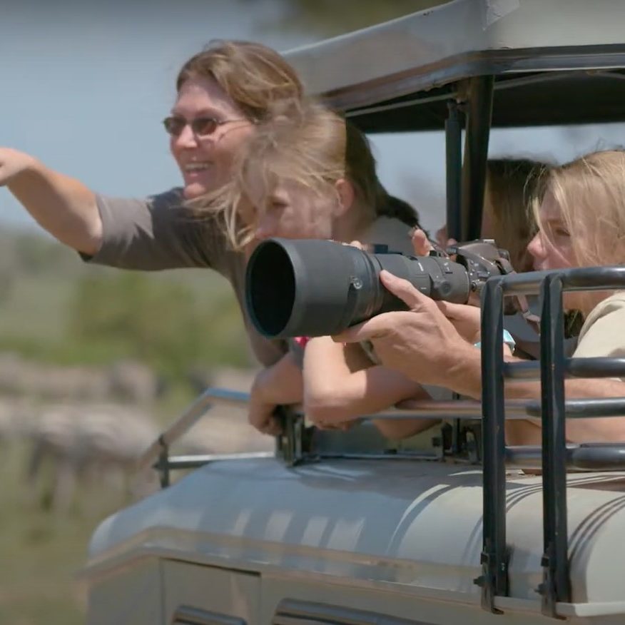 Family enjoying a budget-friendly holiday with kids taking photos on a game drive, affordable accommodations, and scenic views in the background.