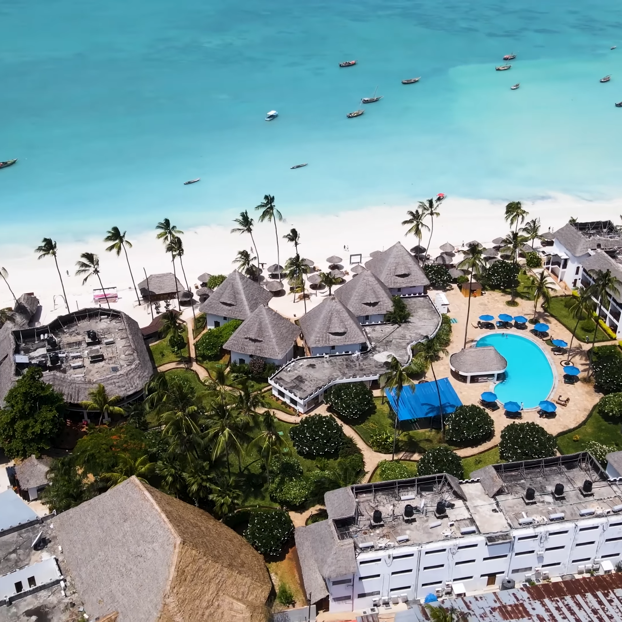 Aerial view of an affordable beach resort in Zanzibar, Tanzania. The resort features white sand, palm trees, and a swimming pool.